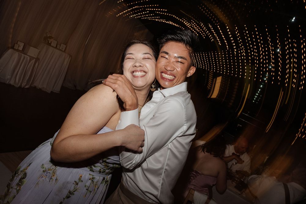 Two joyful guests hugging and smiling on the wedding dance floor surrounded by warm string lights. Captured by Aliza Dworkind at Le Cathcart