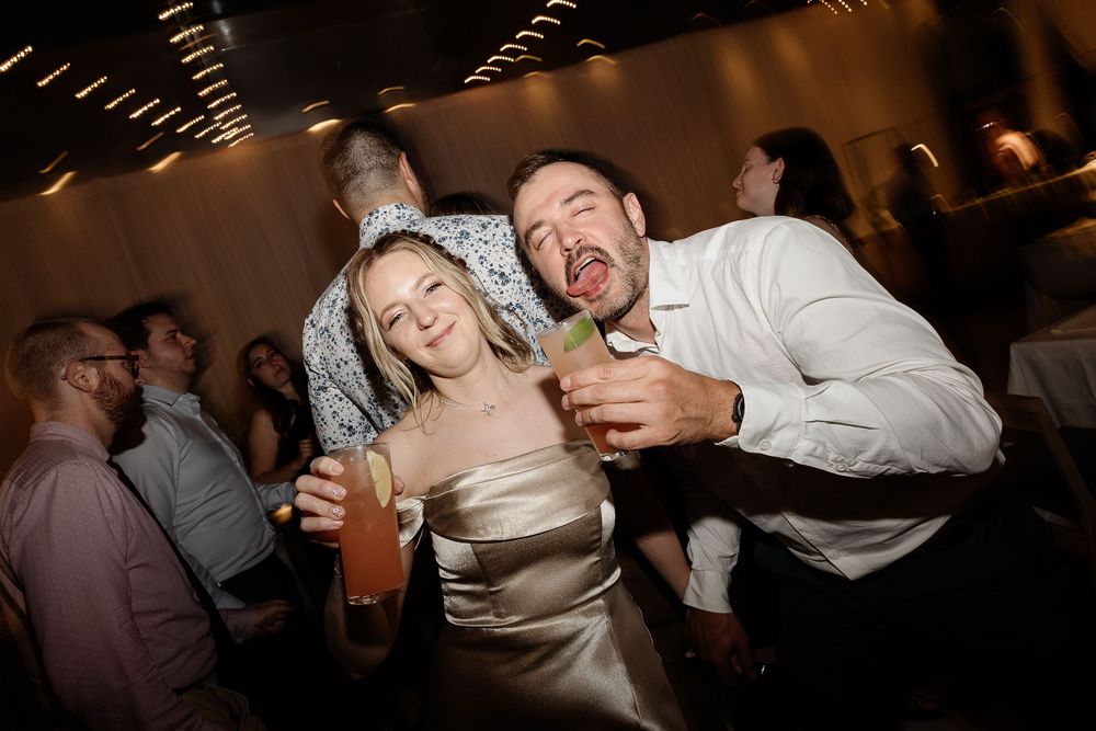 Joyful couple holding cocktails and laughing together at a lively wedding reception party.