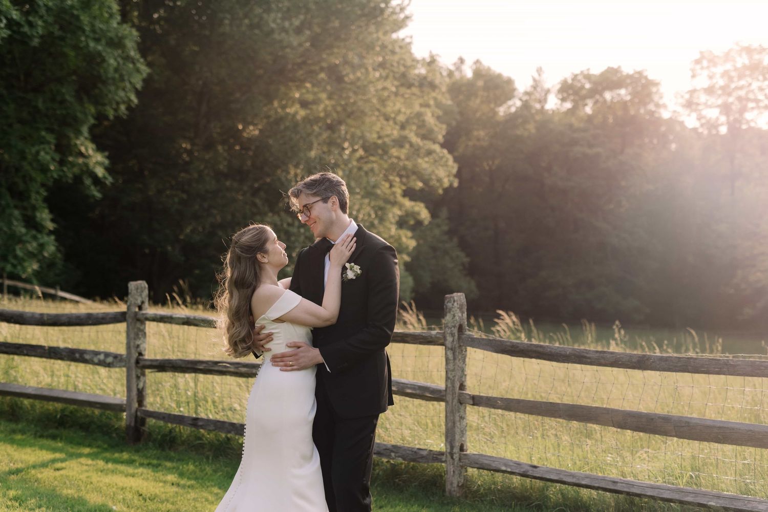 Bride and groom sharing a romantic moment at golden hour by a rustic wooden fence.