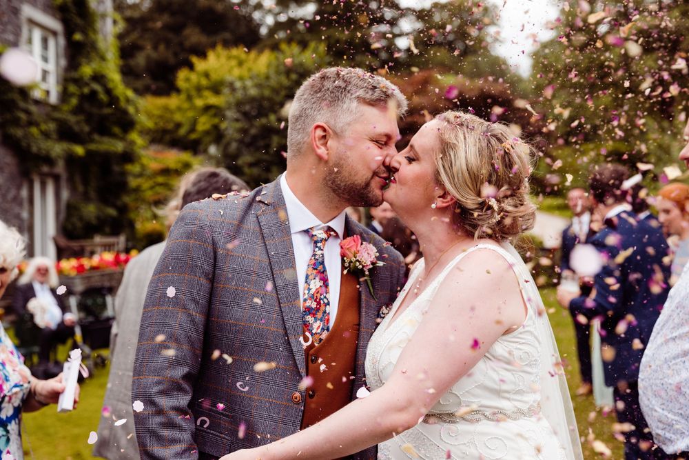 Bride and groom sharing a kiss surrounded by colorful confetti during outdoor wedding celebration.