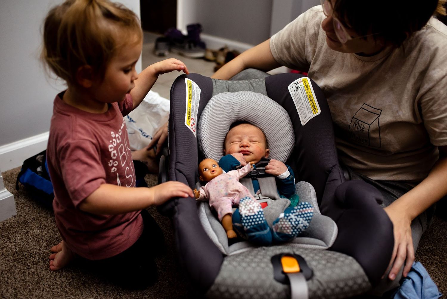 Young child meets new sibling safely secured in infant car seat.
