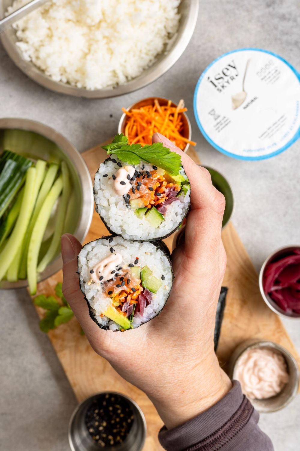 Hand holding two halves of a sushi burrito filled with rice, avocado, carrots, and veggies on a wooden board.