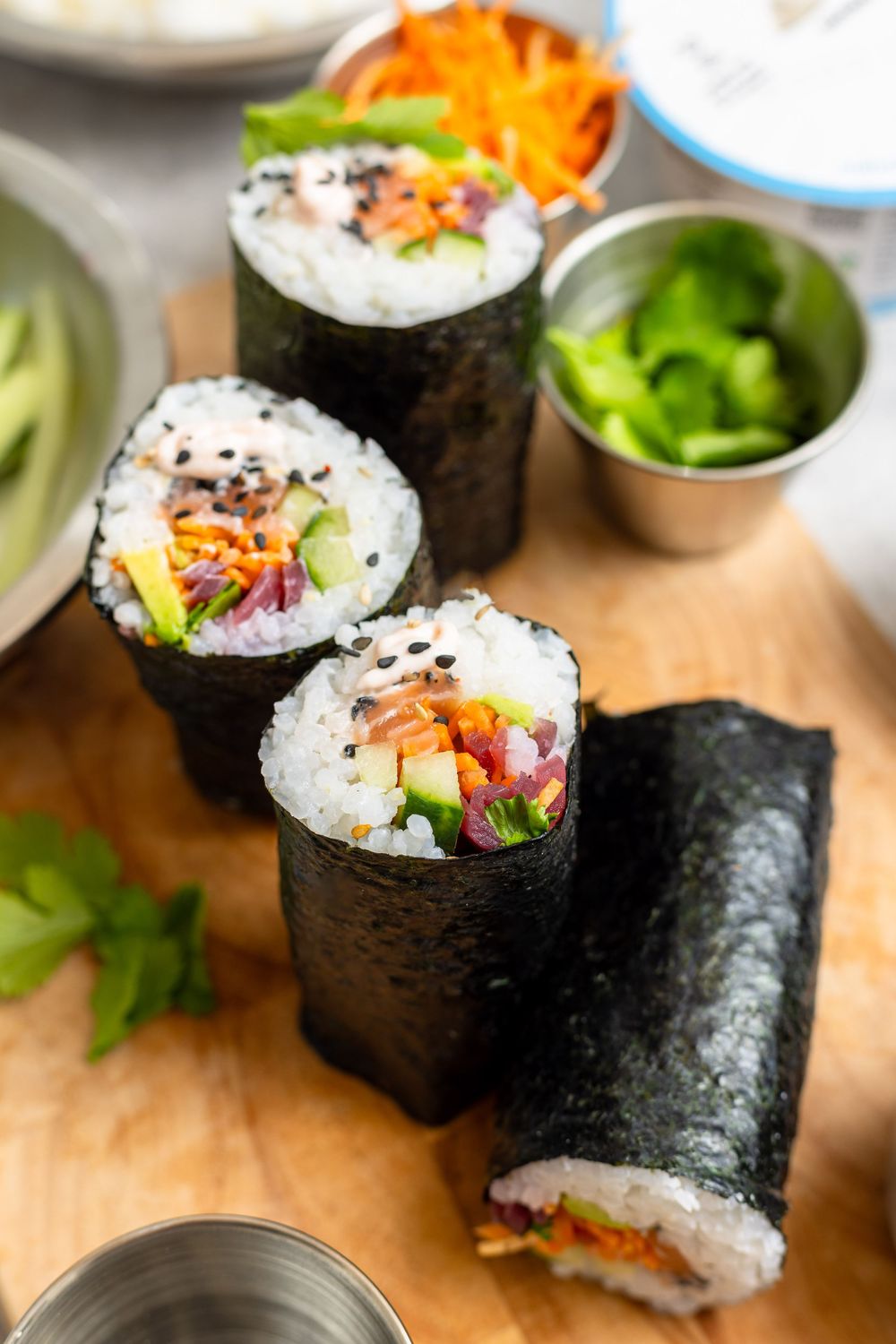 Close-up of four colorful sushi burritos wrapped in nori, filled with rice, carrots, avocado, and vegetables on a wooden board.