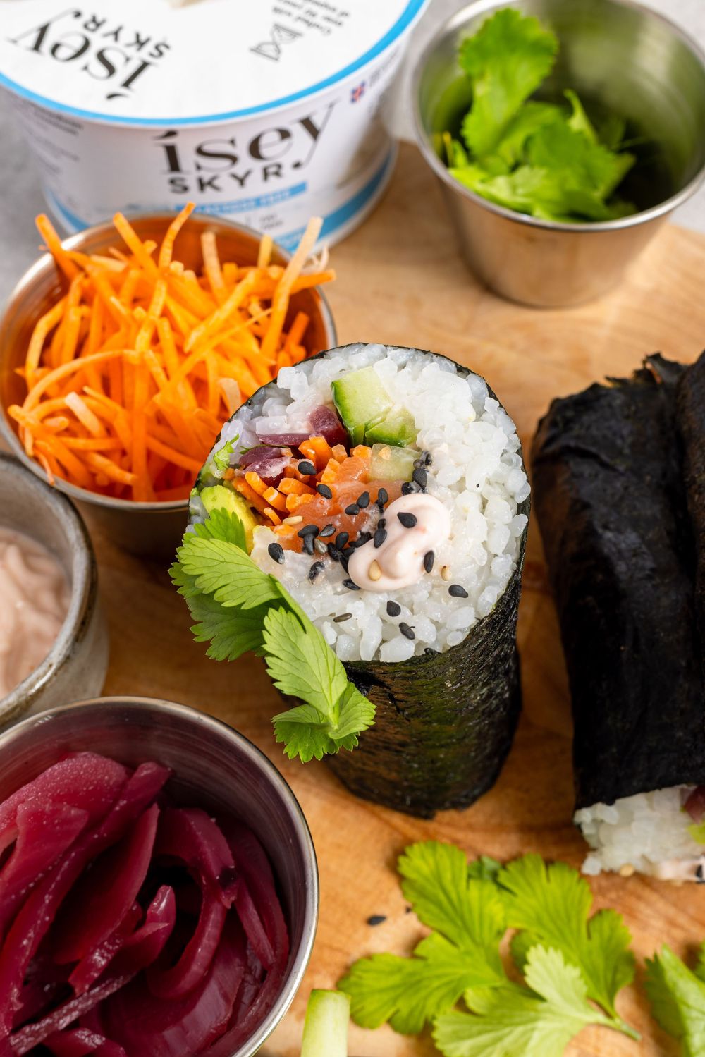 Close-up of a sushi burrito cross-section with rice, avocado, carrots, and Isey Skyr on a wooden board.