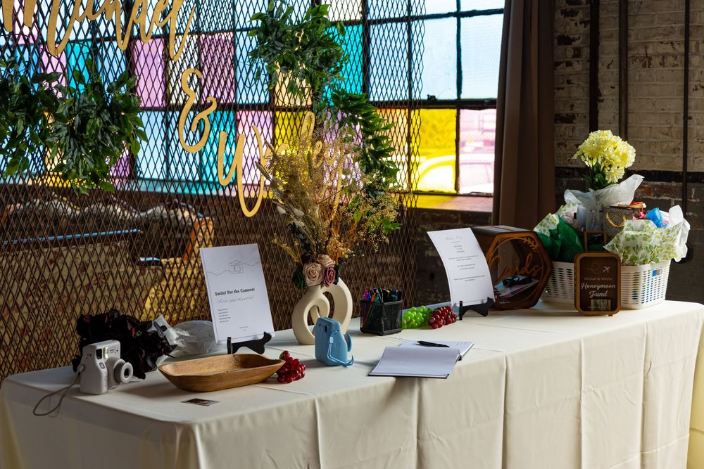 A decorated event table with floral arrangements, signage, and colorful stained glass window backdrop.
