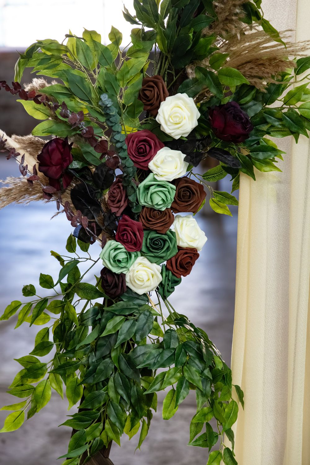 Elegant floral arrangement with dark red, white, and green roses surrounded by lush green foliage for a wedding ceremony.