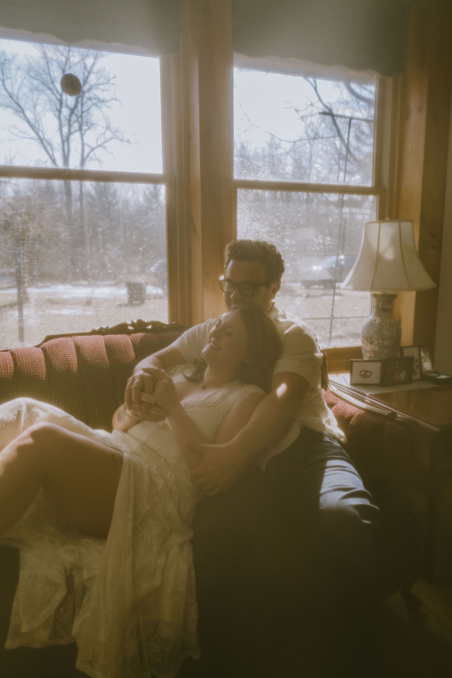 Couple embracing on a couch by a sunlit window in a cozy rustic living room, romantic intimate moment.