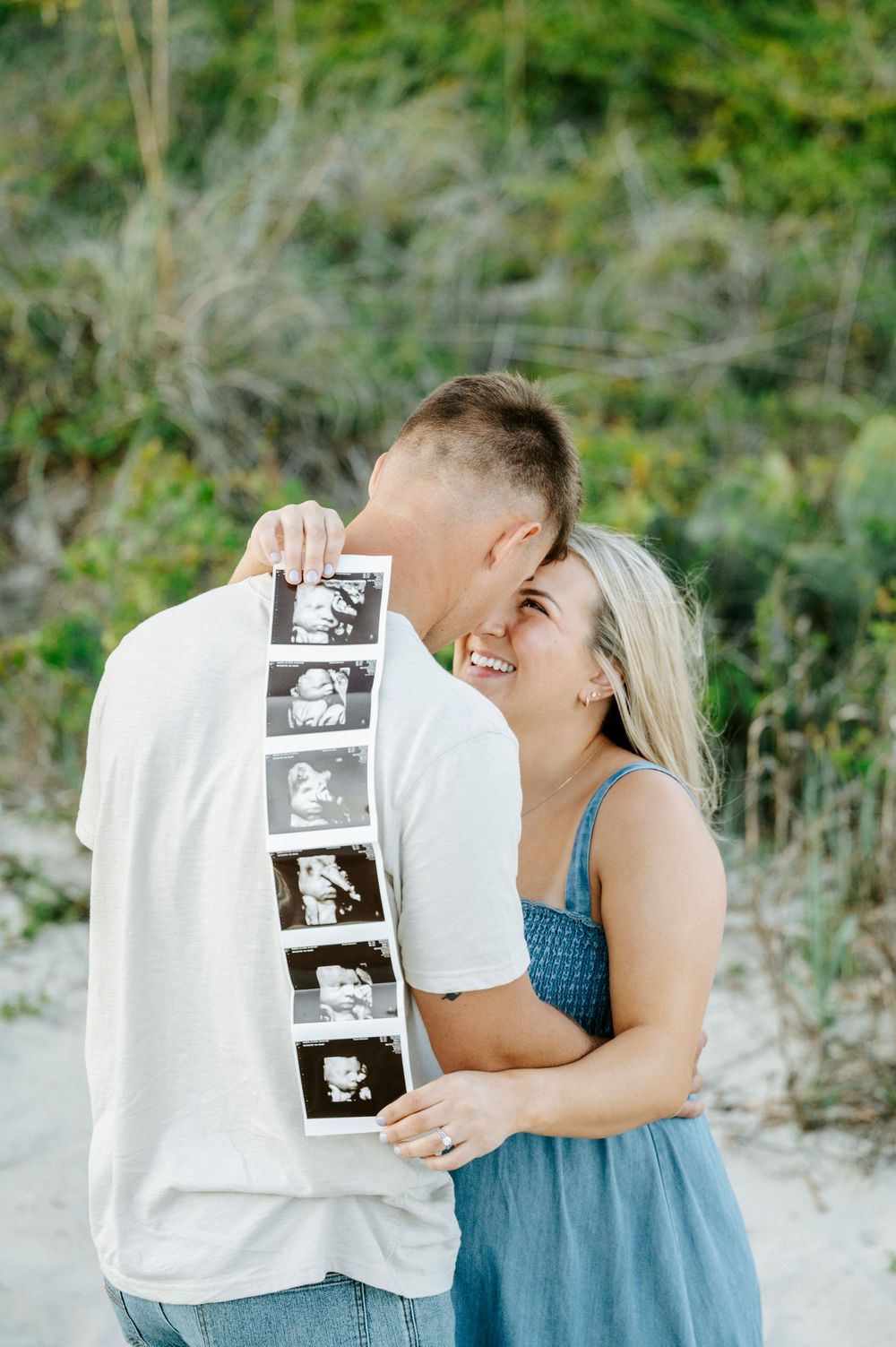 Happy couple holding ultrasound photos outdoors, smiling and embracing during a pregnancy announcement photoshoot.