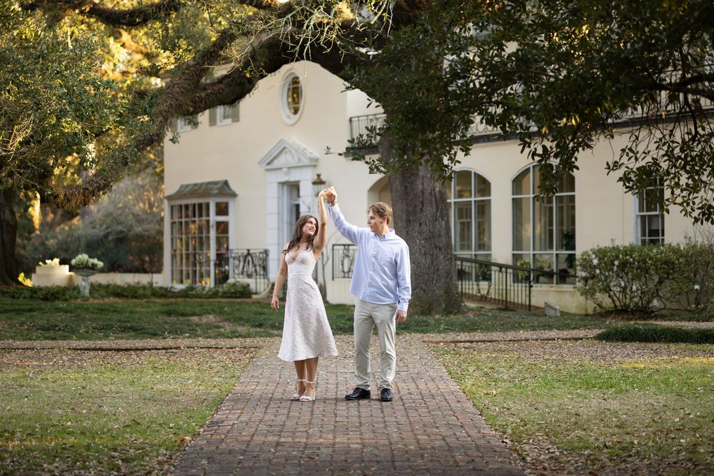 Couple dancing on brick path before white Southern estate surrounded by oak trees.