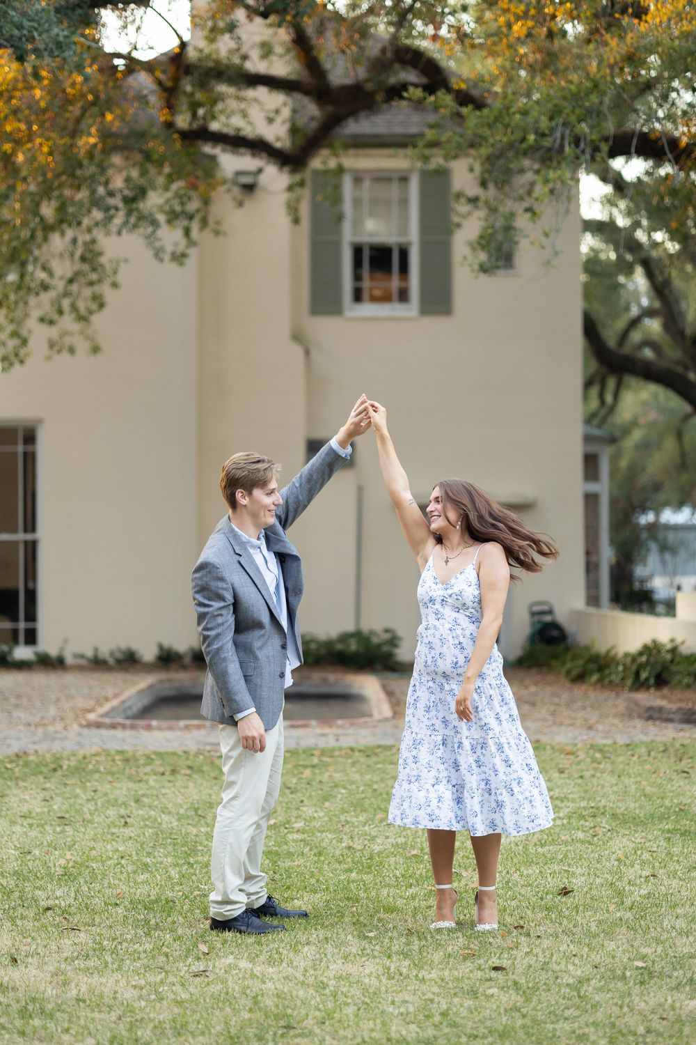 Joyful couple dancing outdoors as man twirls woman in floral dress on green lawn.