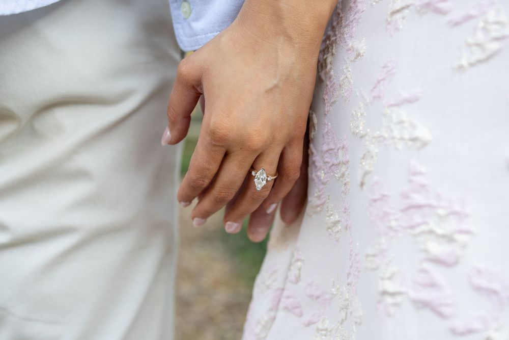 Close-up of a bride wearing a stunning diamond engagement ring on her wedding day, with lace dress detail visible.