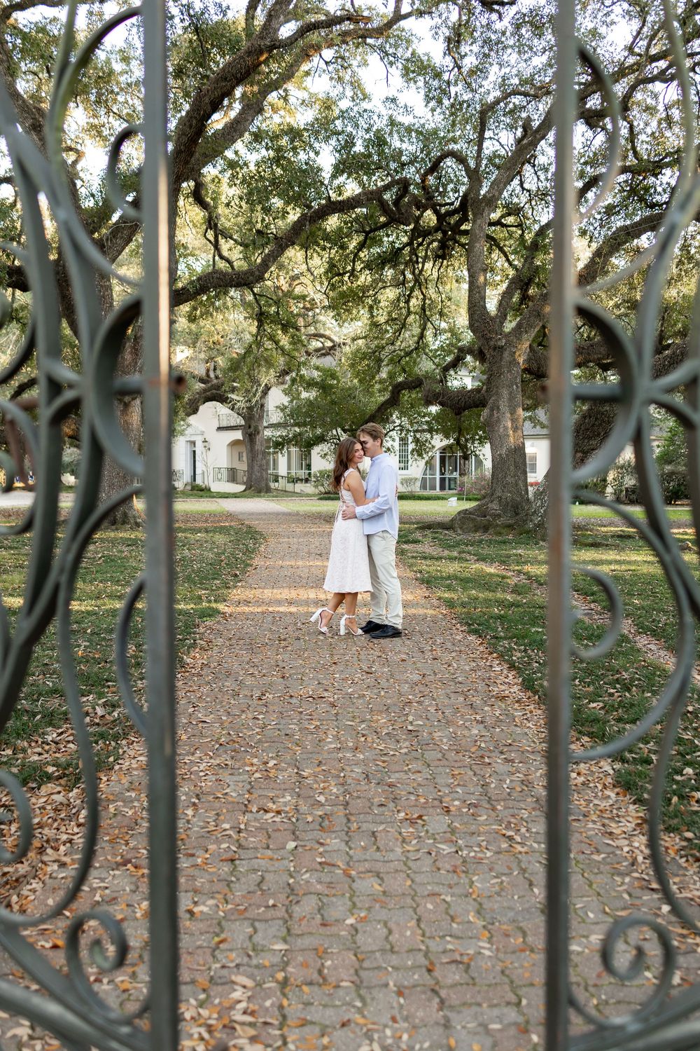 Couple embracing on a garden path framed by ornate wrought iron gates.