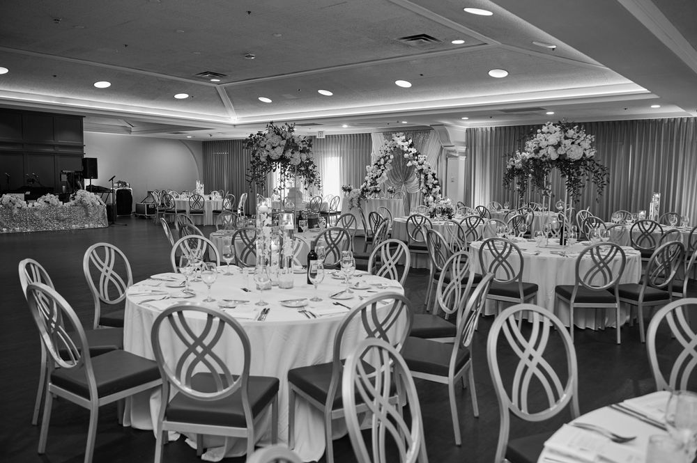 Elegant black and white photo of a banquet hall with round tables, floral centerpieces, and decorative chairs set for a wedding reception.