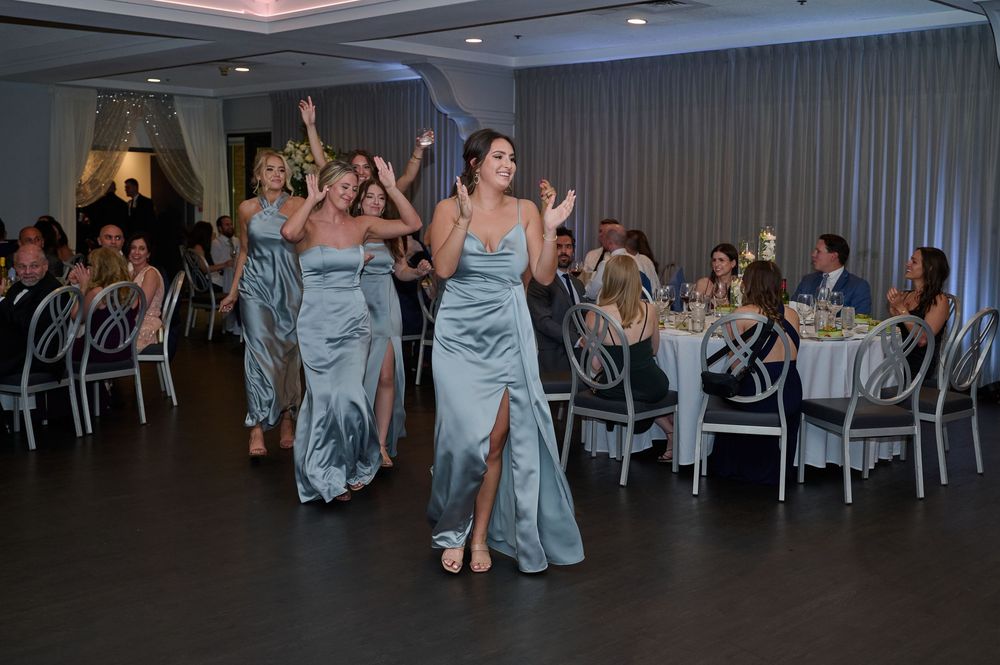Bridesmaids in silver satin gowns make a joyful entrance at an elegant wedding reception.