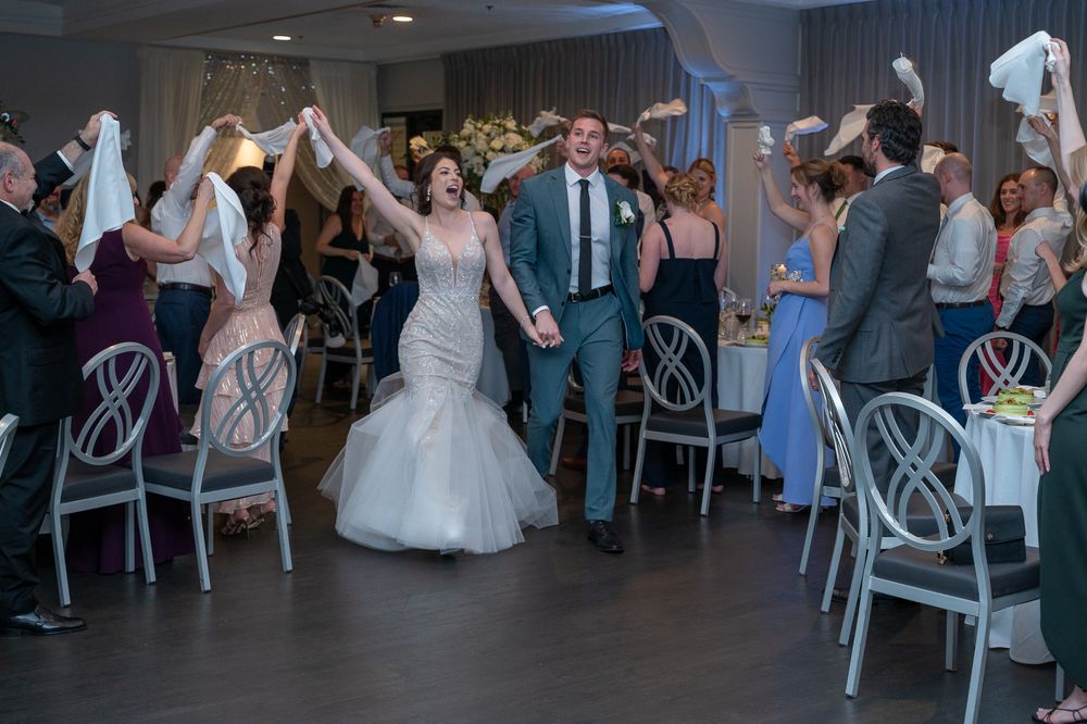 Bride and groom make grand entrance at wedding reception as guests wave white napkins in celebration.