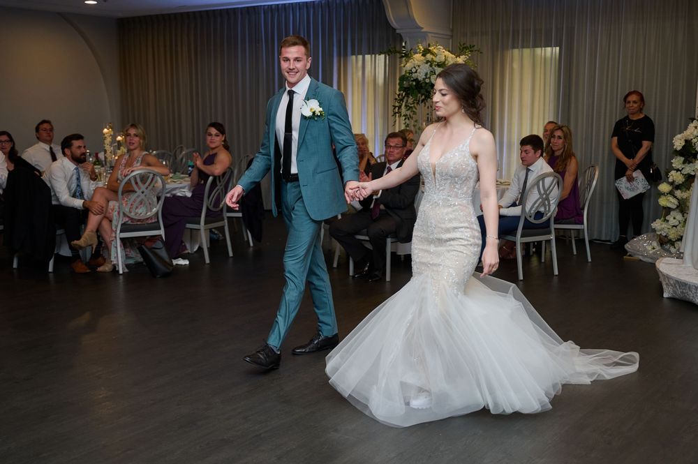 Bride in mermaid gown and groom in teal suit share their first dance at wedding reception.