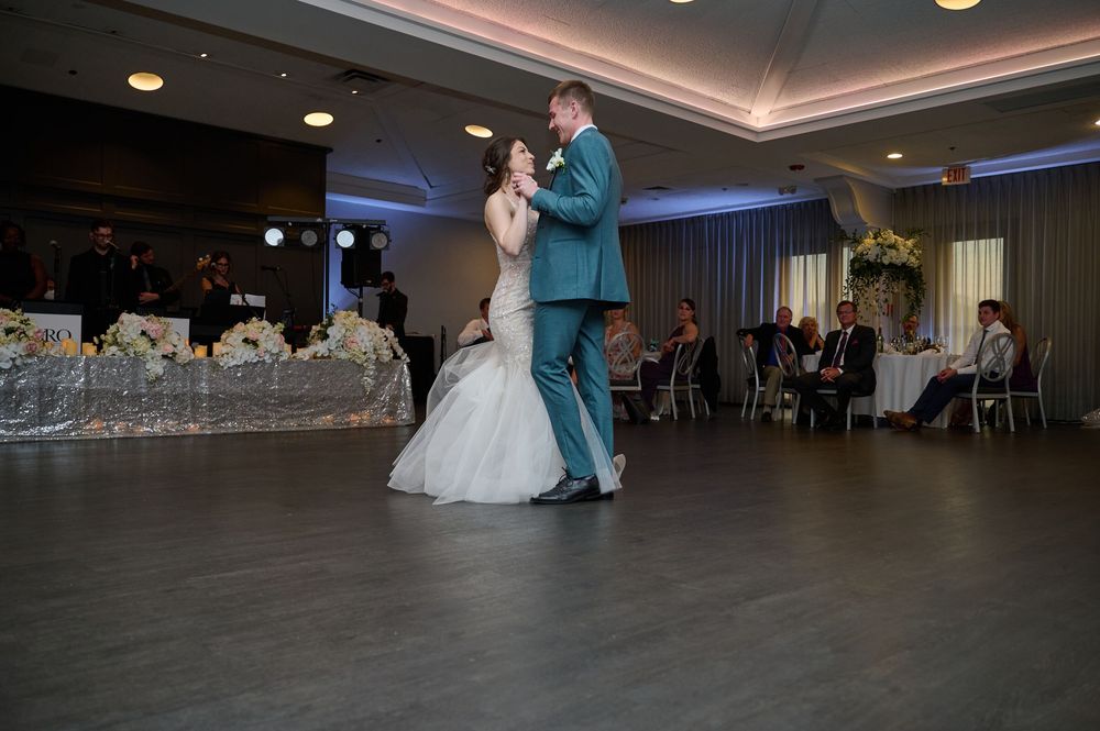 Bride and groom share their first dance at a wedding reception in an elegant ballroom with guests seated nearby.