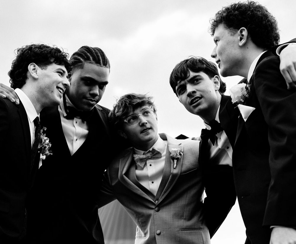 Five young men in formal suits pose together in a black and white photo at a prom or formal event.