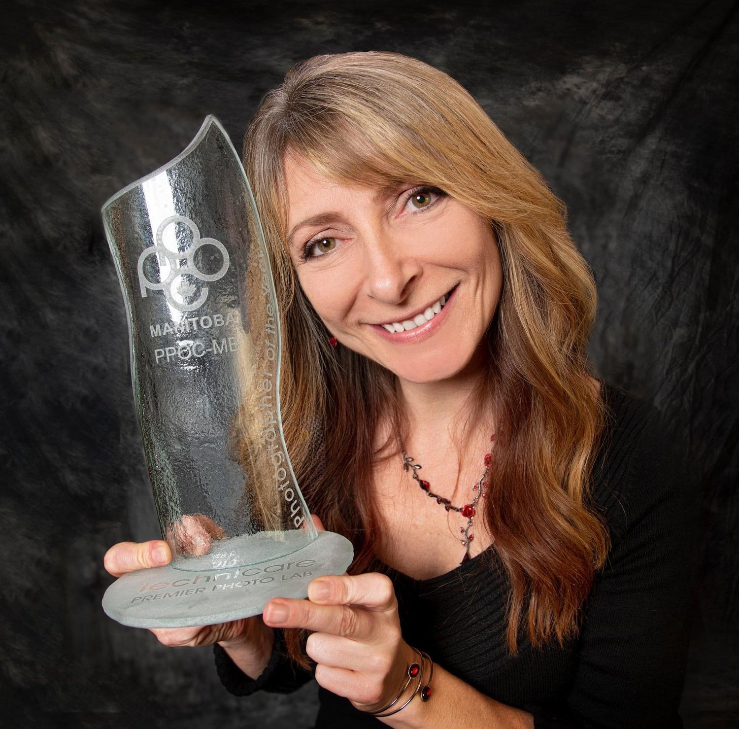 Candice Daum holding clear glass Photographer of the Year trophy award against dark background.