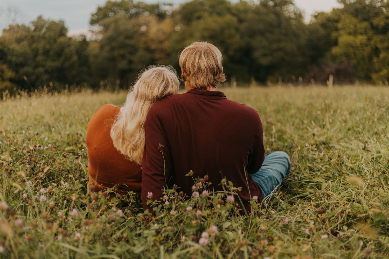 Couple in burgundy sweaters lying together in autumn field.