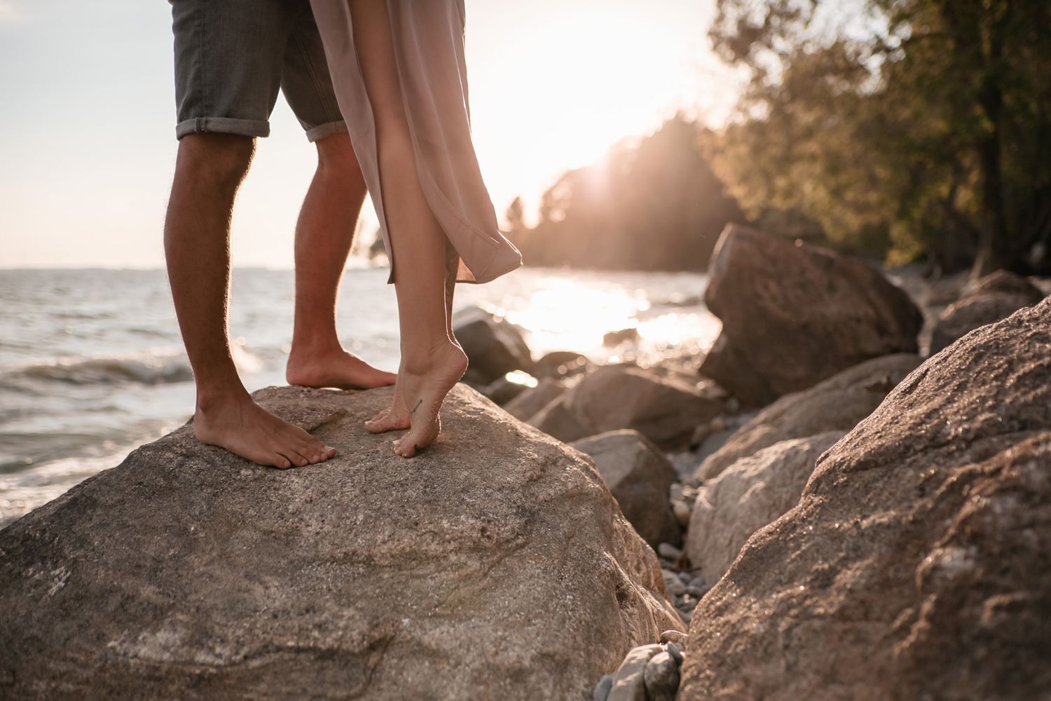 Detail shot of a couple's legs and feet standing on a rock on a limestone beach during golden hour in Kingston, Ontario.