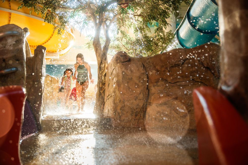 Splashing water sprays through the air at a water park on a sunny summer day with trees in the background.