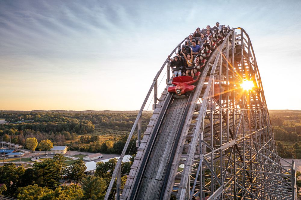Thrilling roller coaster track with dramatic sunlit sky at sunset in an amusement park.