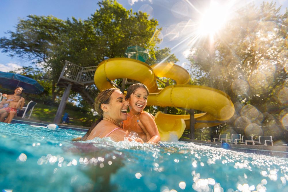 People enjoying a refreshing swim at a water park with yellow water slides and bright sunlight streaming through the trees.