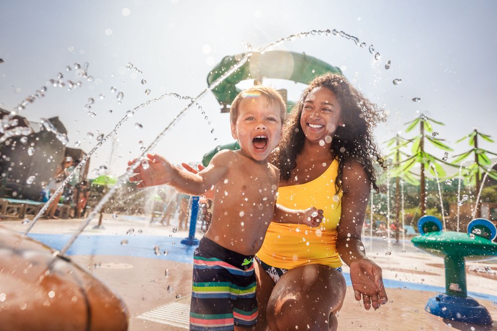 Children splashing and playing in water sprinklers at an outdoor water park on a sunny day.