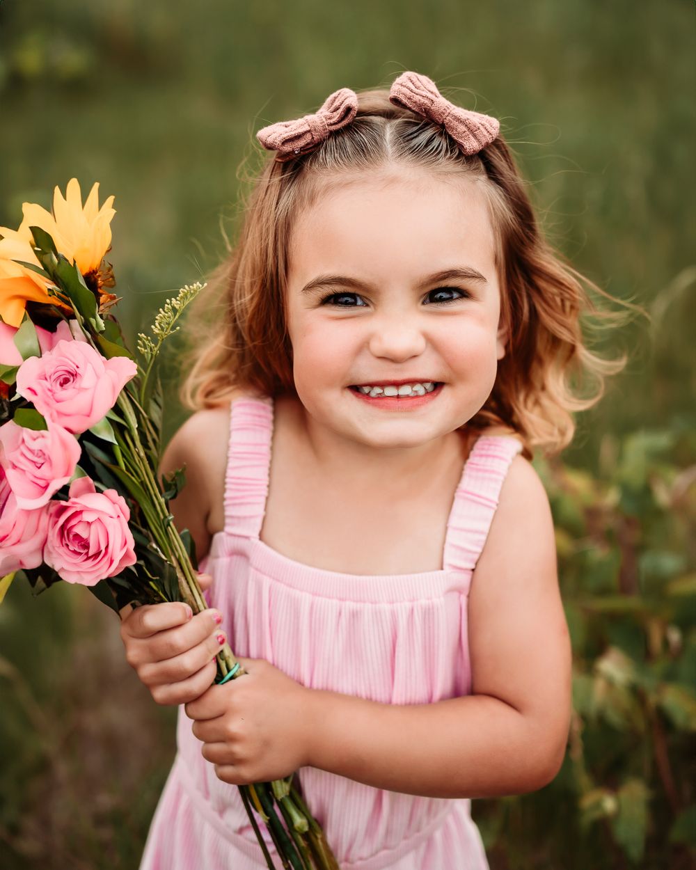 Pink dress and hair bows holding colorful flower bouquet in garden setting.