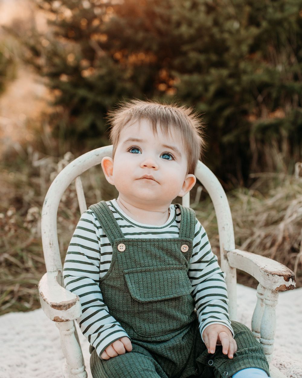 Green corduroy overalls and striped shirt in white chair outdoor portrait.