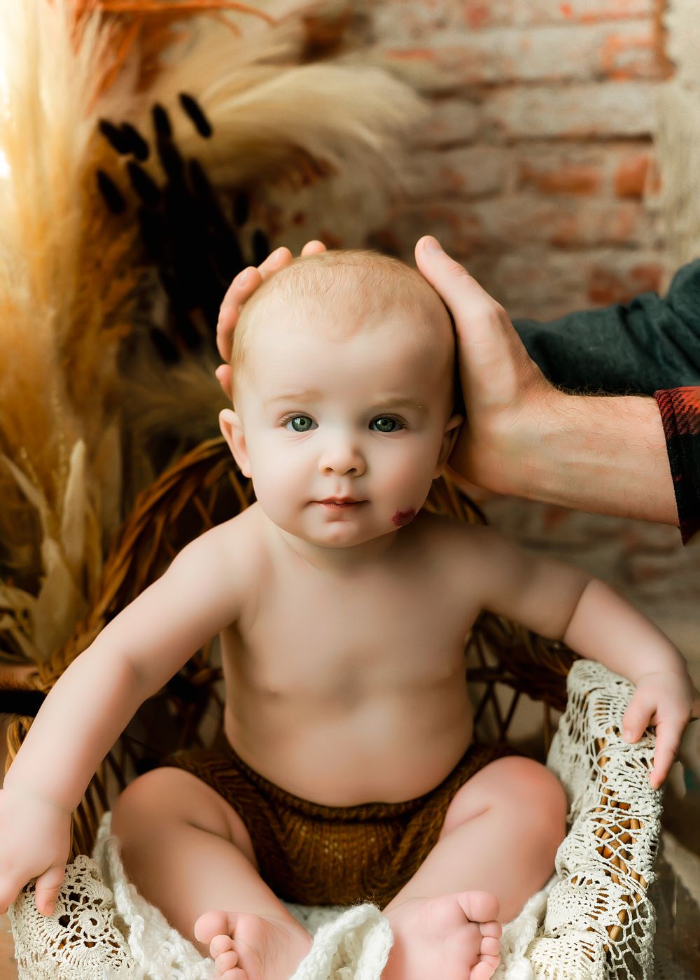Professional portrait of infant in rustic setting with pampas grass and brick wall backdrop.