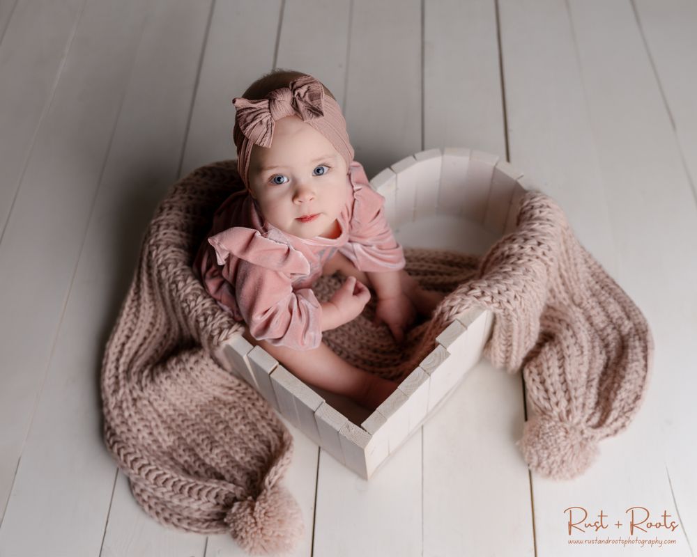 Professional portrait of baby in knit blanket and wooden box setup.