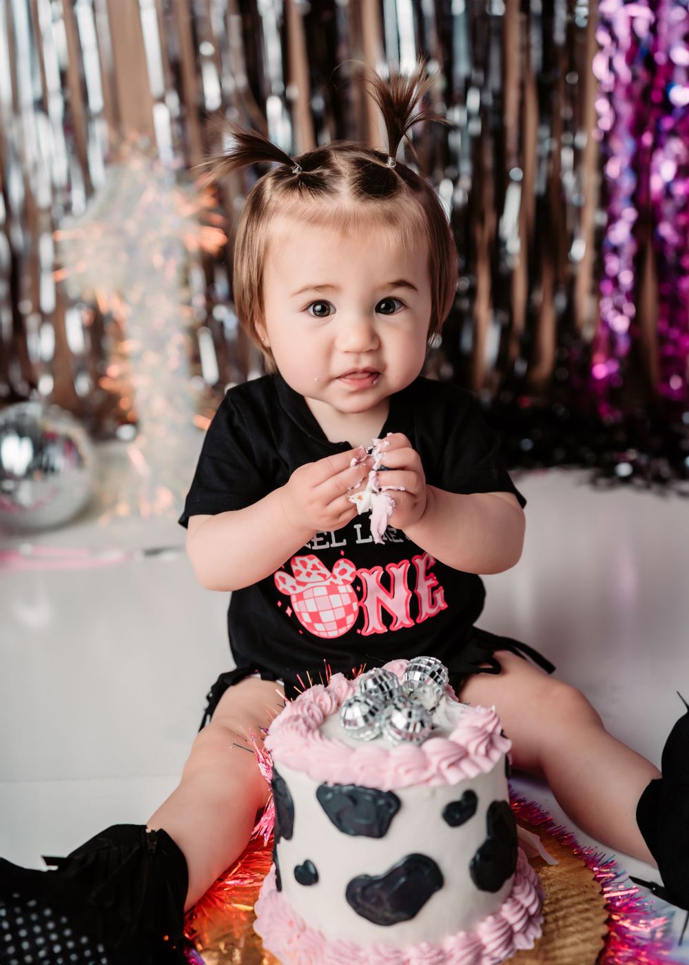 Toddler in black outfit sits with birthday cake featuring cow print design.