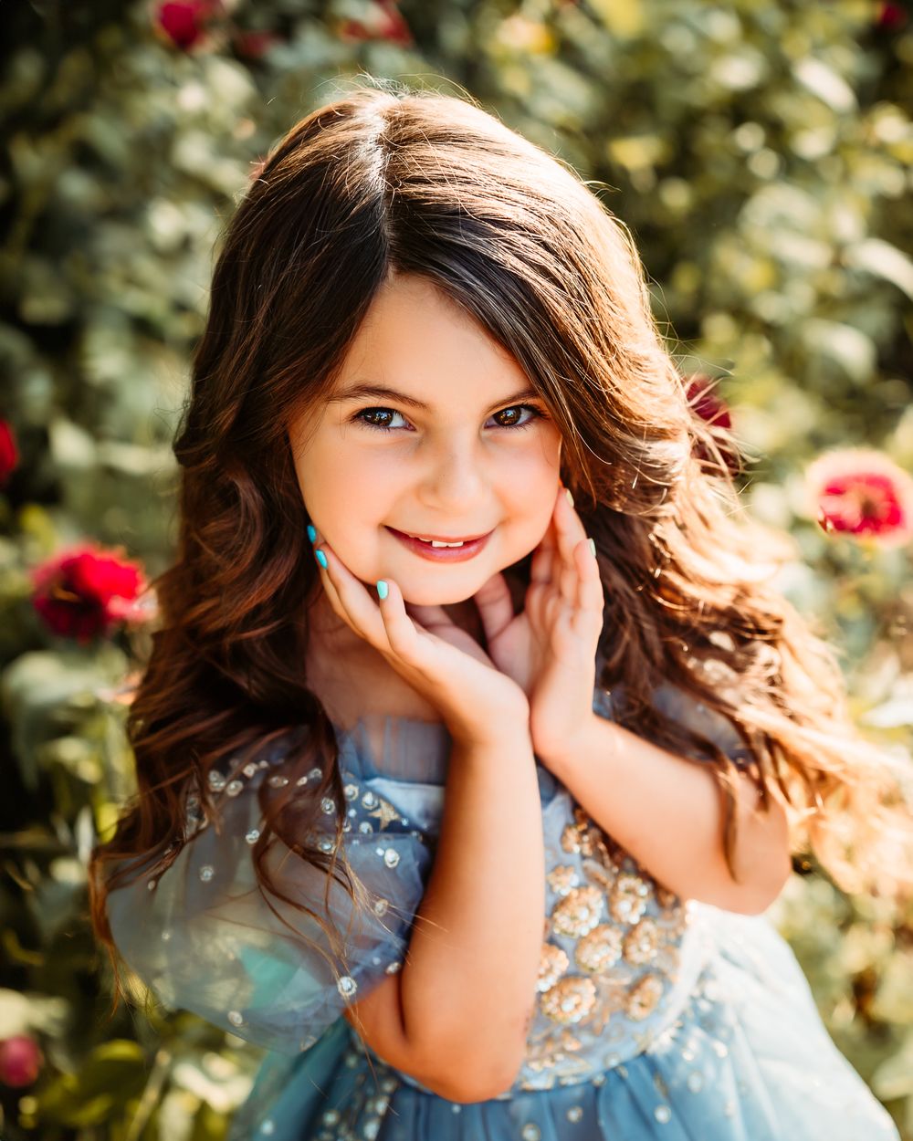 Garden portrait with red roses wearing blue floral dress.