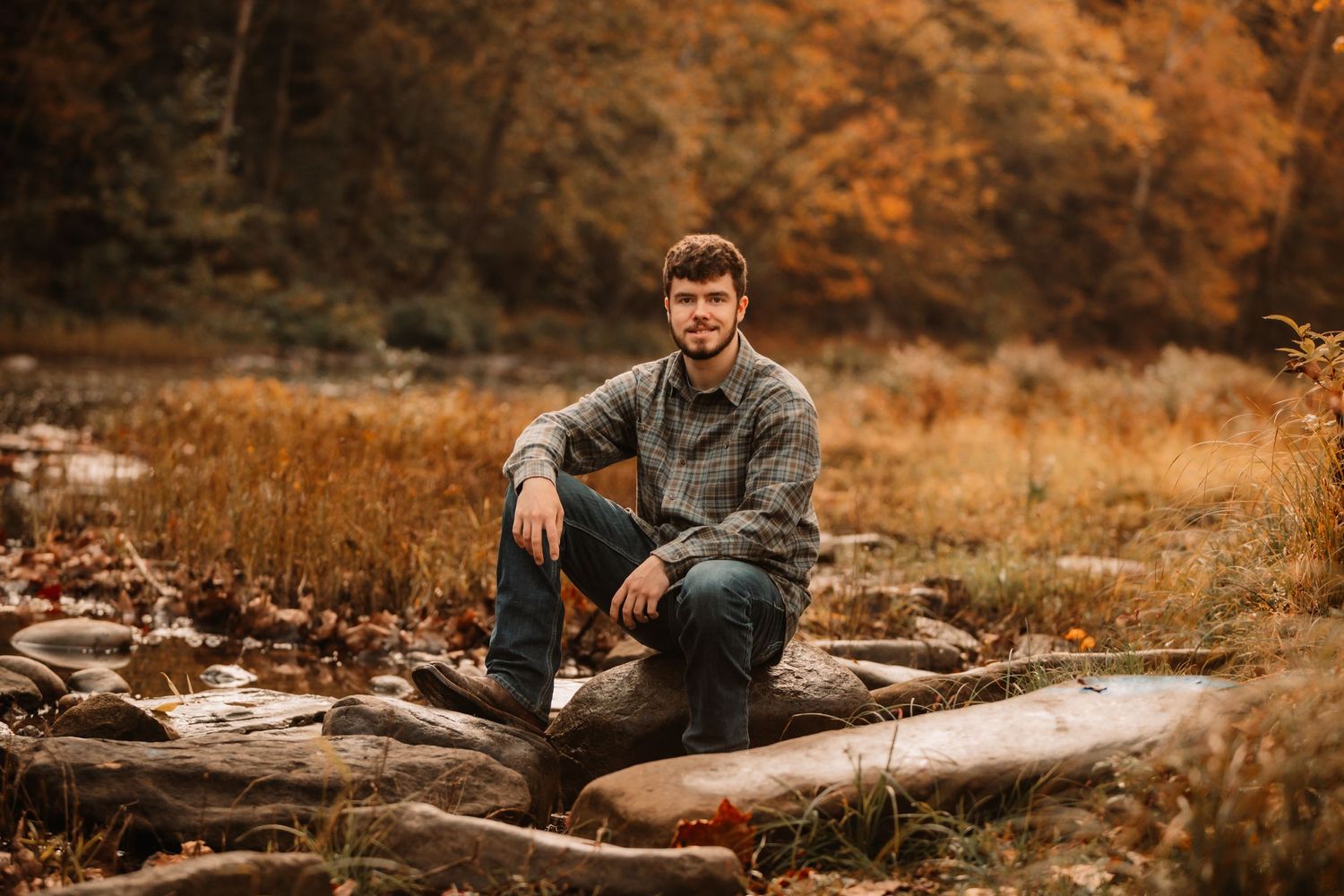 Person in grey sweater sits casually on fallen log in autumn woodland setting.