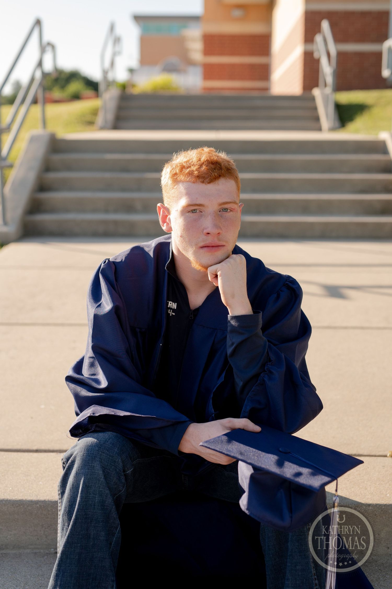 Student in dark graduation attire poses thoughtfully on outdoor stairs.