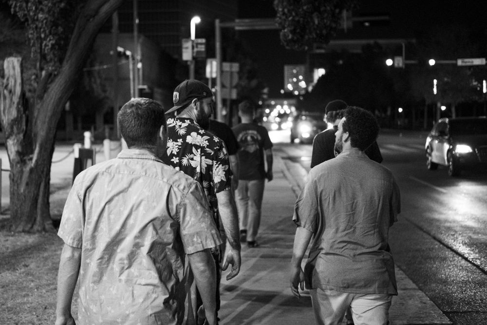 Black and white street scene of people walking on an urban sidewalk at night.