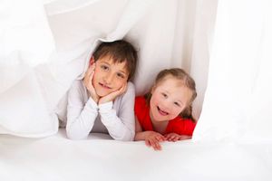 Deux enfants se regardent sous des couvertures blanches en riant.