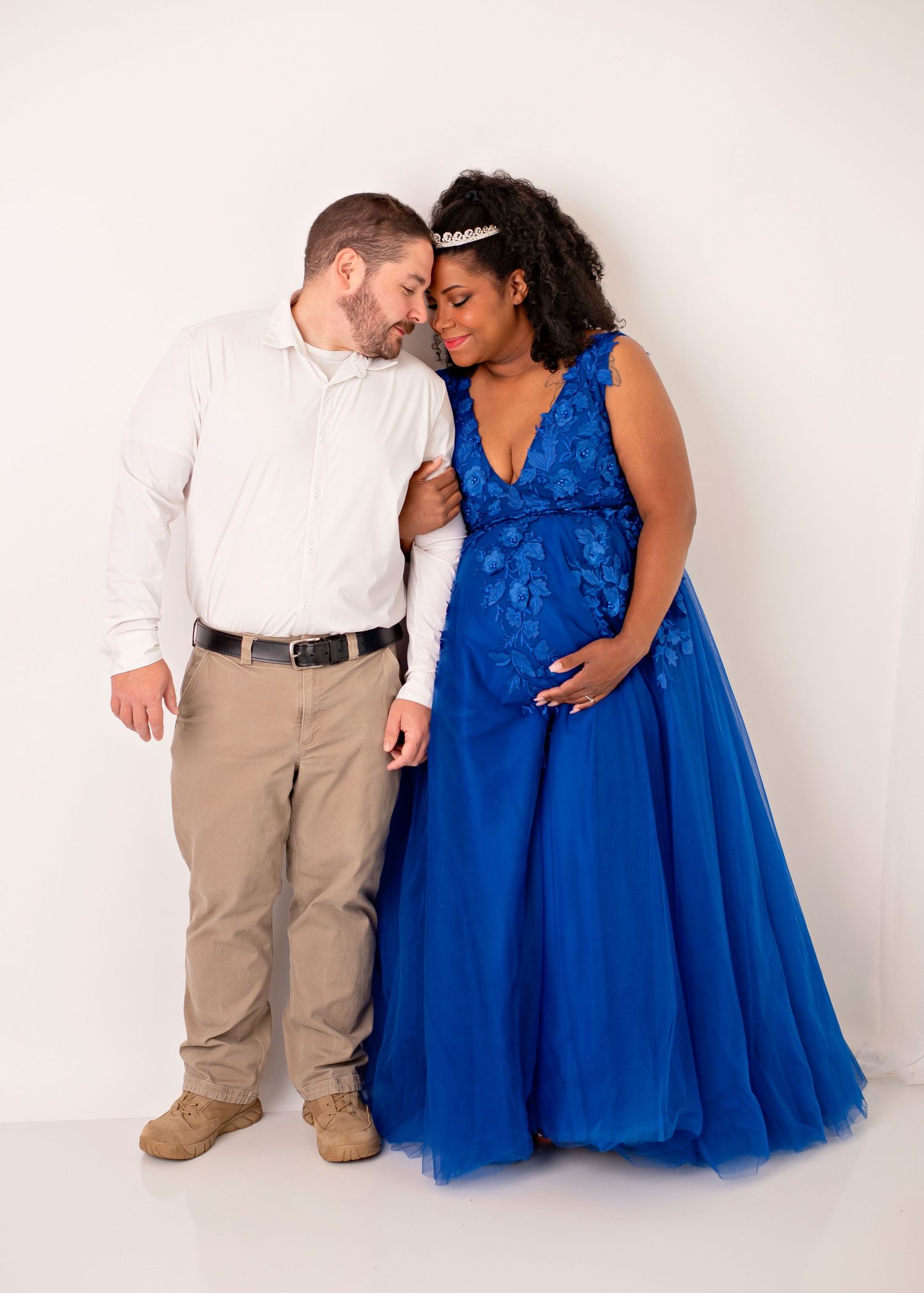 Expecting mother in royal blue floor-length gown poses against white studio background.