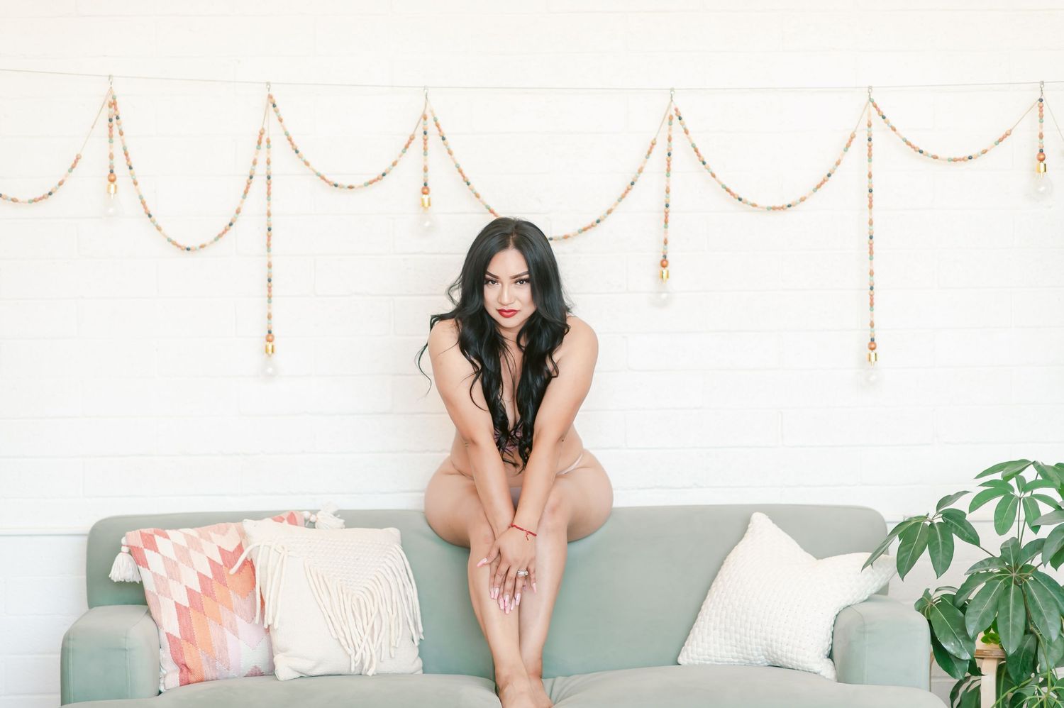 A boudoir photoshoot features a woman in white lingerie posing against a light backdrop with floral decorations.