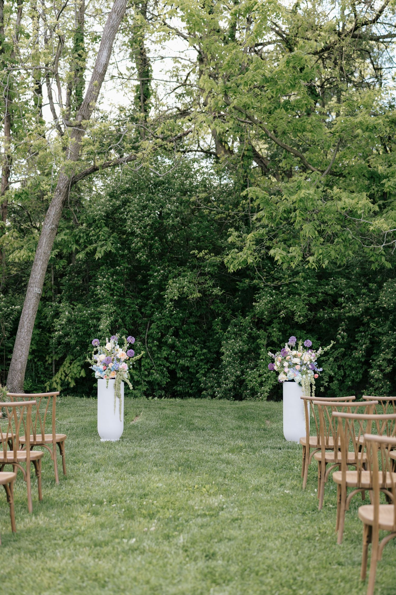 A group of groomsmen in black suits share a candid laughing moment together outdoors under trees.