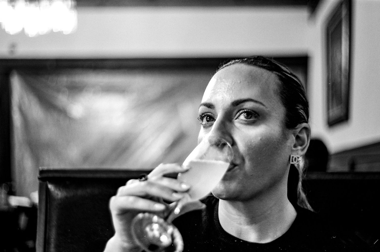 Black and white close-up of a person drinking from a stemmed glass.