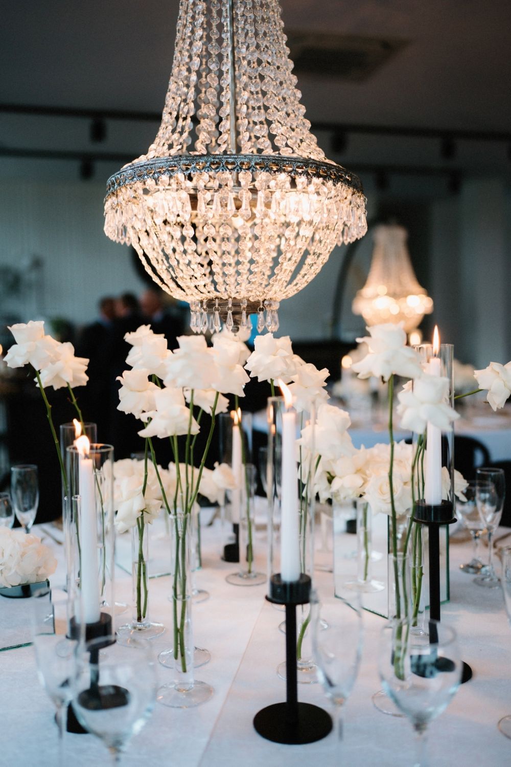 Crystal chandeliers hang above white floral centerpieces on elegant wedding reception tables.