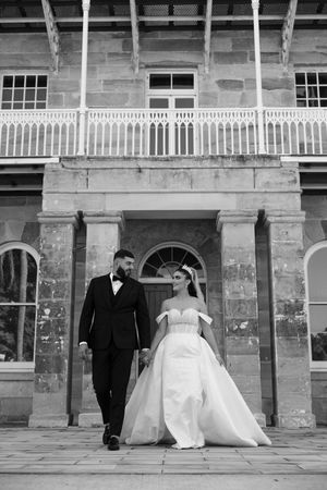 Black and white portrait of couple walking outside historic colonial building with classic architecture.