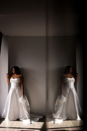 Artistic bridal portrait with mirror reflection showing white wedding gown in dramatic lighting.