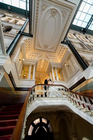 Ornate white staircase with red carpet in a grand historic building featuring elegant architectural details and high ceilings.