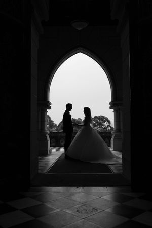 Silhouette of wedding couple framed by gothic archway in dramatic black and white composition.