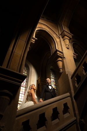 Dramatic lighting captures newlyweds on ornate staircase inside historic church interior.