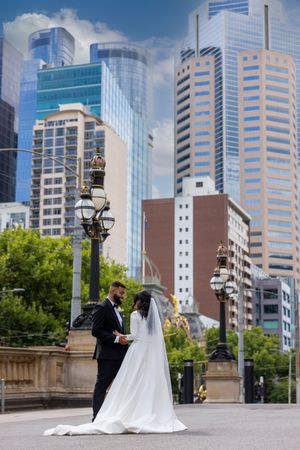Wedding couple posing on city steps with modern skyscrapers and ornate lamp posts in the background.